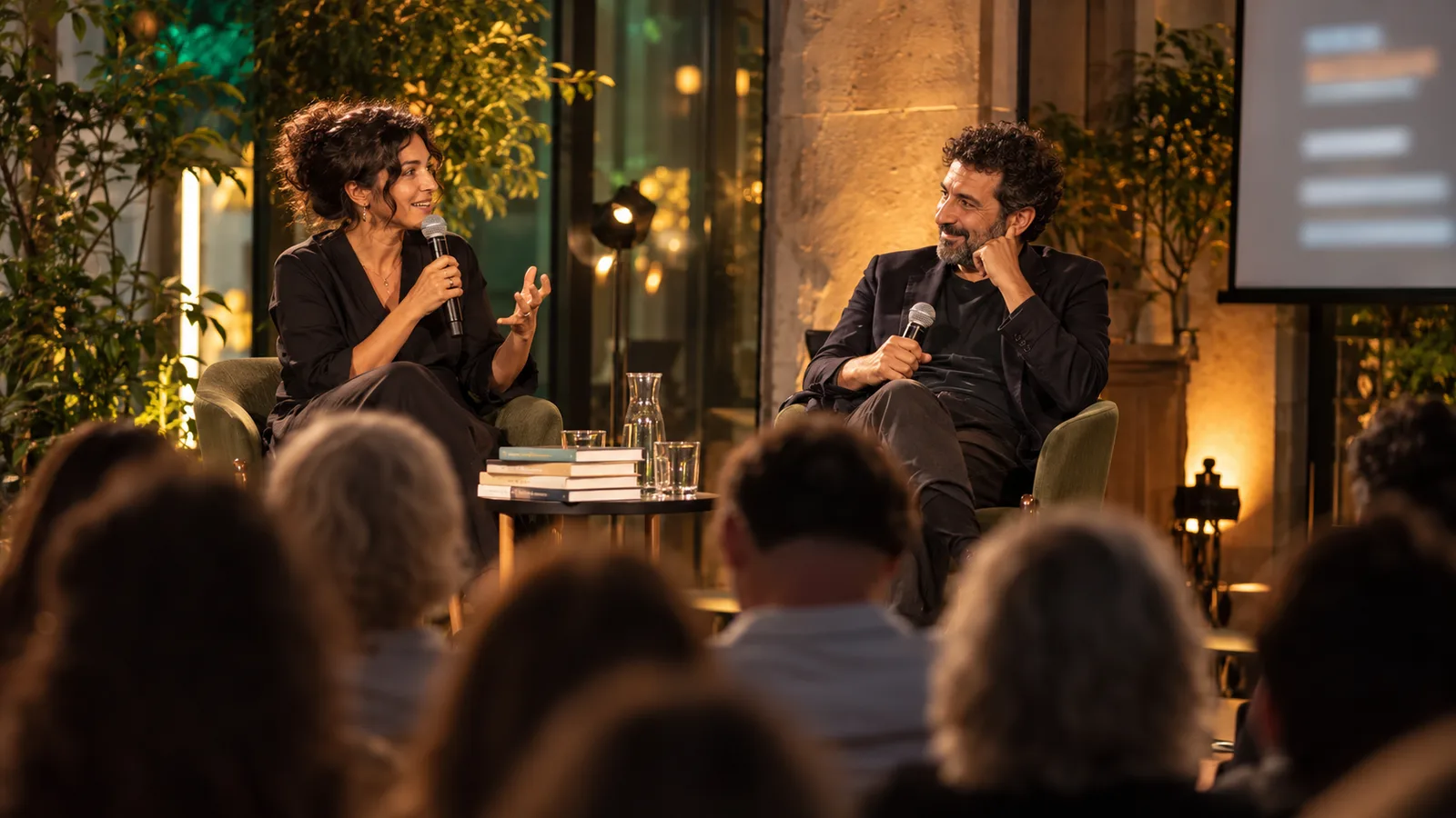 Zwei Personen sprechen mit Mikrofonen bei einem Literaturabend vor Publikum.